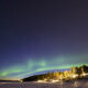 Un pueblo nevado a oscuras bajo el destello de una aurora boreal.